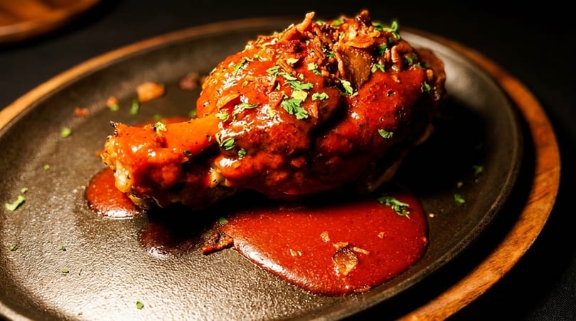 A chicken drumstick covered in red sauce and herbs on a dark skillet.