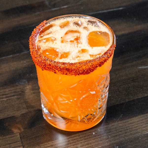 Vibrant orange cocktail with a chili-salt rim and ice in a cut glass.