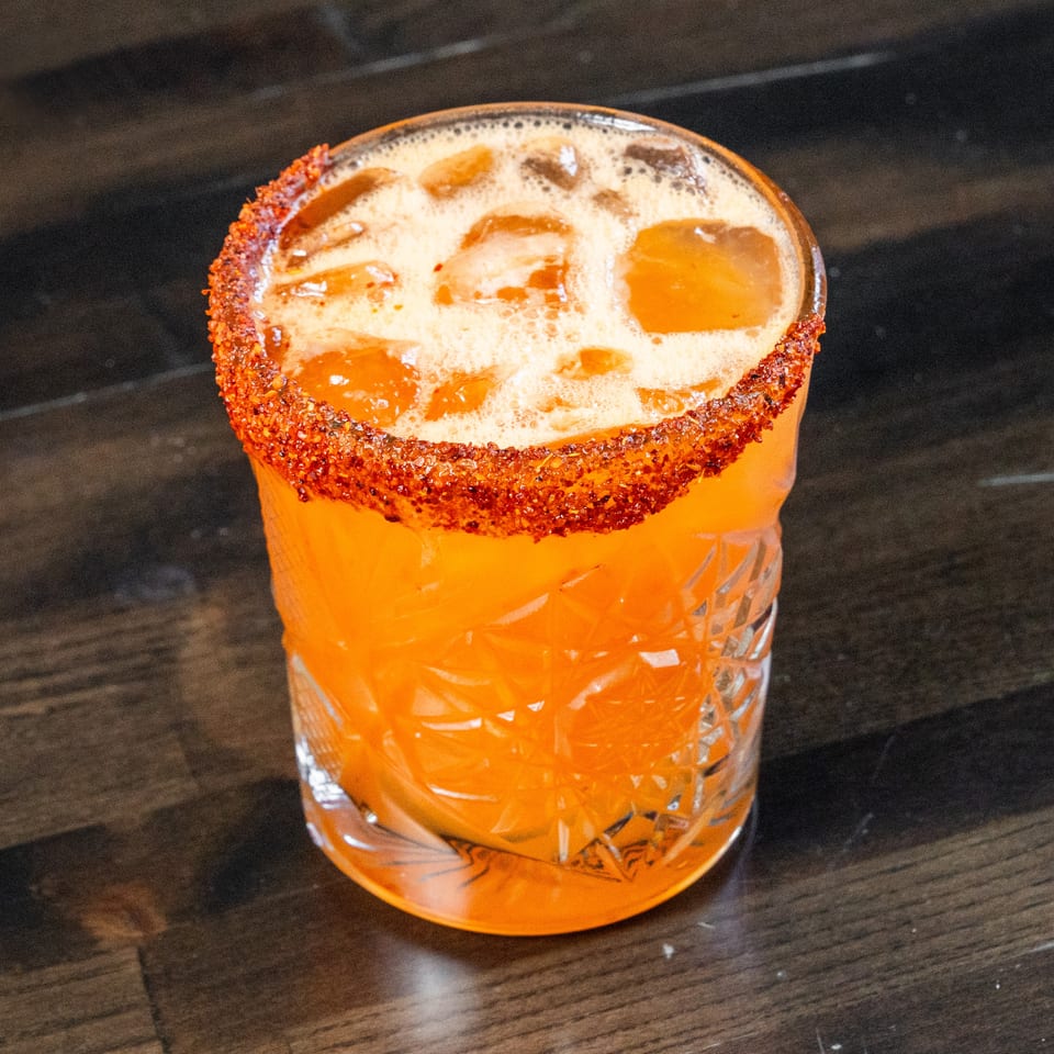 Vibrant orange cocktail with a chili-salt rim and ice in a cut glass.