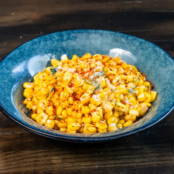 A blue bowl filled with seasoned corn, topped with cheese and red chili flakes.
