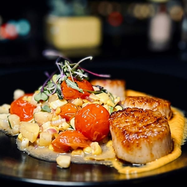 Seared scallops with corn and cherry tomato relish, garnished with microgreens on a black plate.