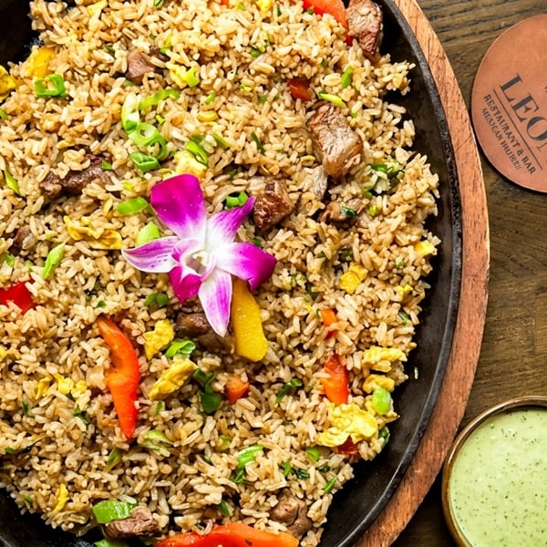 Peruvian fried rice with beef, vegetables, and a purple orchid, served with green sauce.