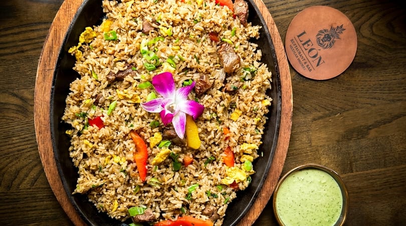Peruvian fried rice with beef, vegetables, and a purple orchid, served with green sauce.