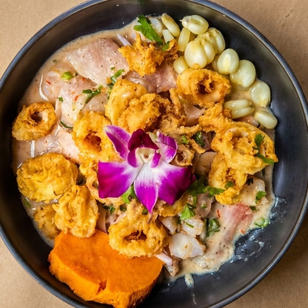 Ceviche with fried calamari, corn, and sweet potato, garnished with a purple orchid.